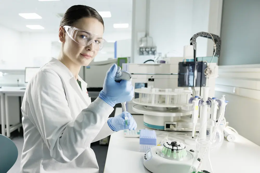 عالمة تجري تجارب في المختبر ، مرتدية معطف المختبر ونظارات السلامة.