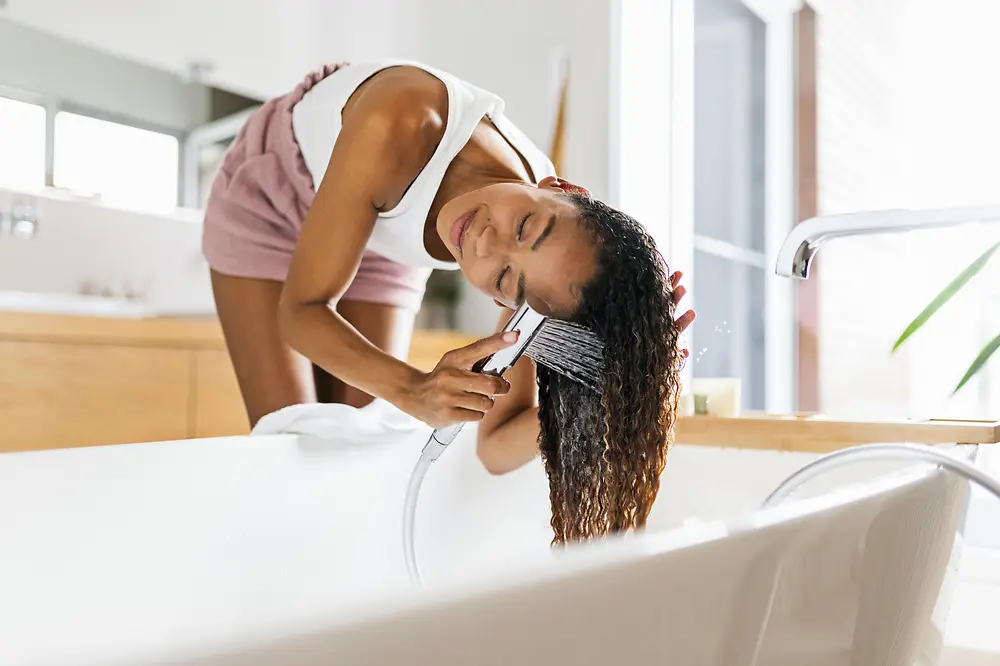 Woman in bathroom washing her brown long hair in bath tube