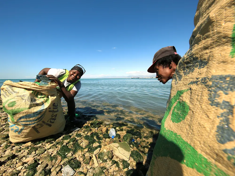 مشروع البنك البلاستيكي: شخصان يجمعان البلاستيك على الشاطئ.