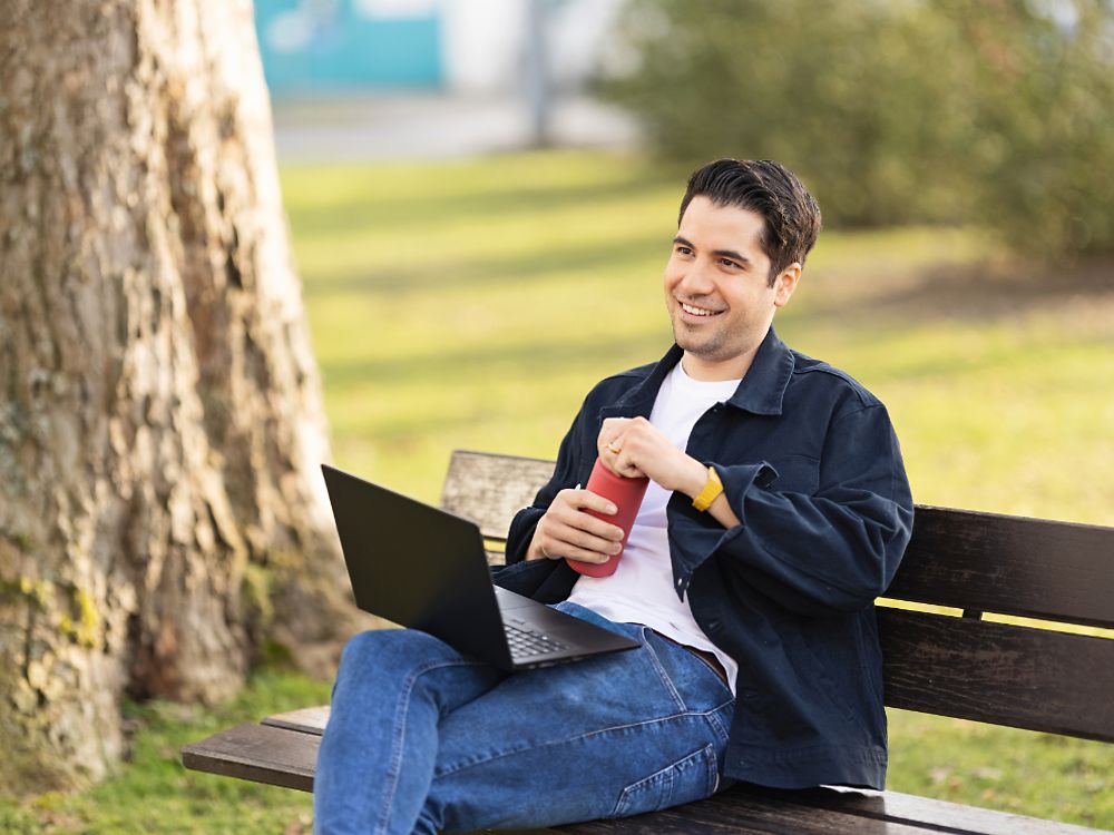 أحد موظفي Henkel يجلس على مقعد في الحديقة ويعمل على حاسوبه المحمول.