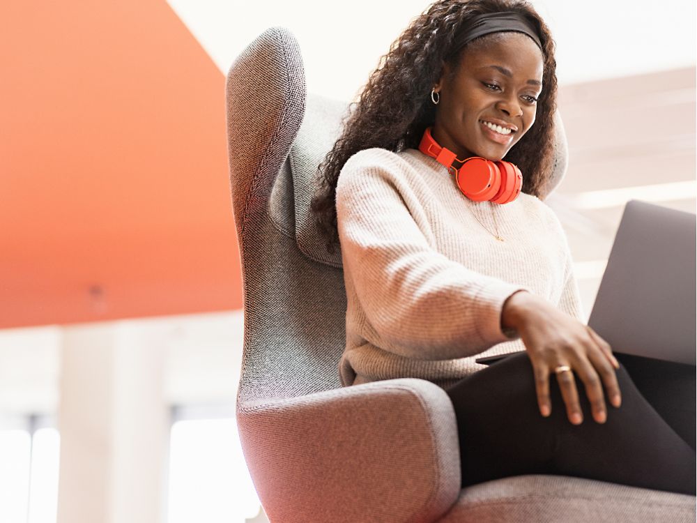إحدى موظفات Henkel تجلس في مقعد مريح وحاسوبها المحمول على ساقيها. إنها تبتسم.