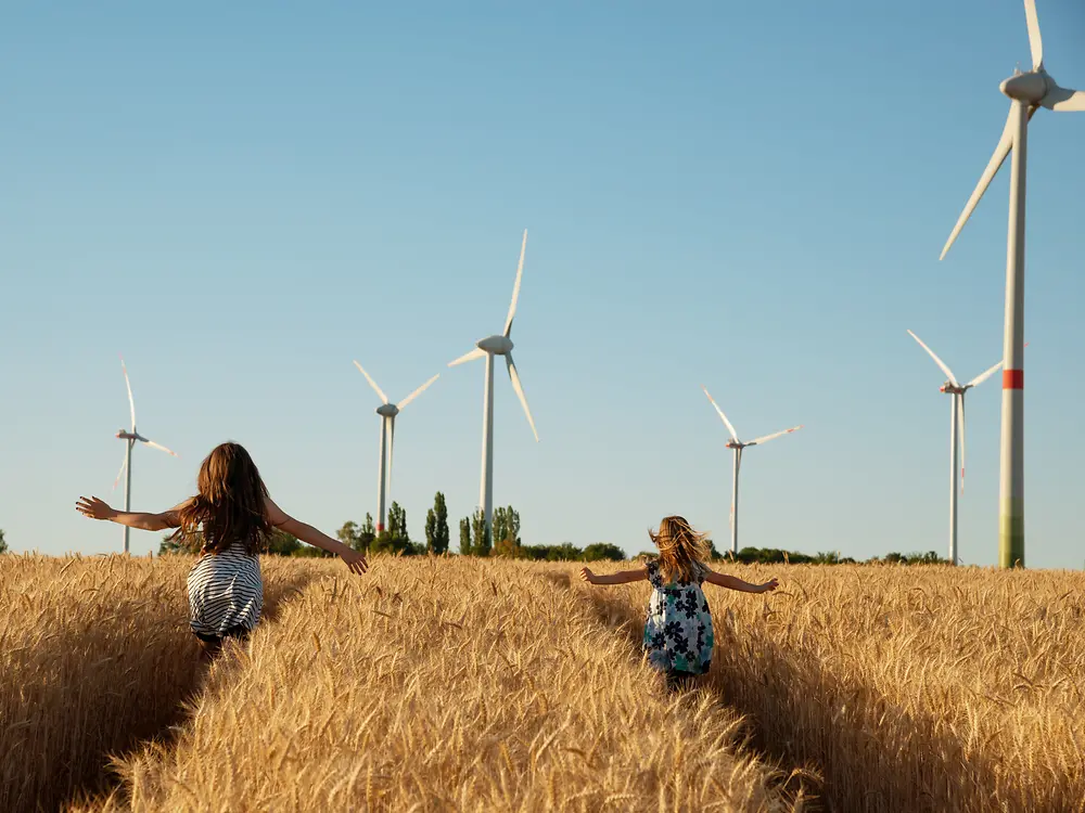 فتيات يركضن عبر حقل نحو أجهزة توليد الطاقة من الرياح.