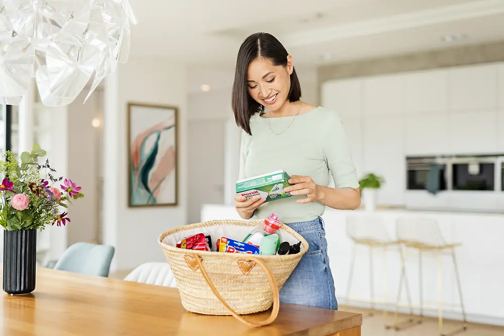 A woman is standing at a dining table holding Persil Power Bars in her hand. 